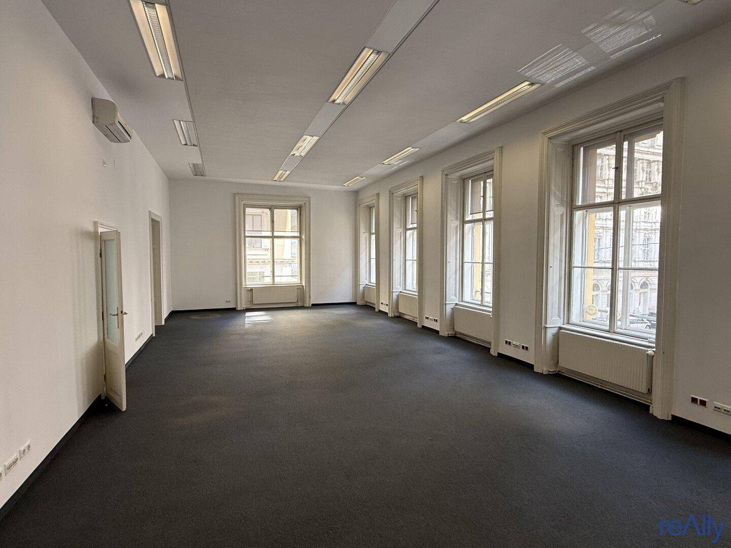 Großes, leeres Büro mit Teppichboden, vielen Fenstern und Klimaanlage, bereit zur individuellen Gestaltung.