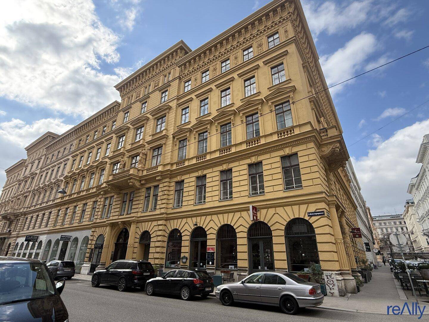 Historisches Eckgebäude mit beeindruckender Architektur, vielen Fenstern und Geschäften im Erdgeschoss.