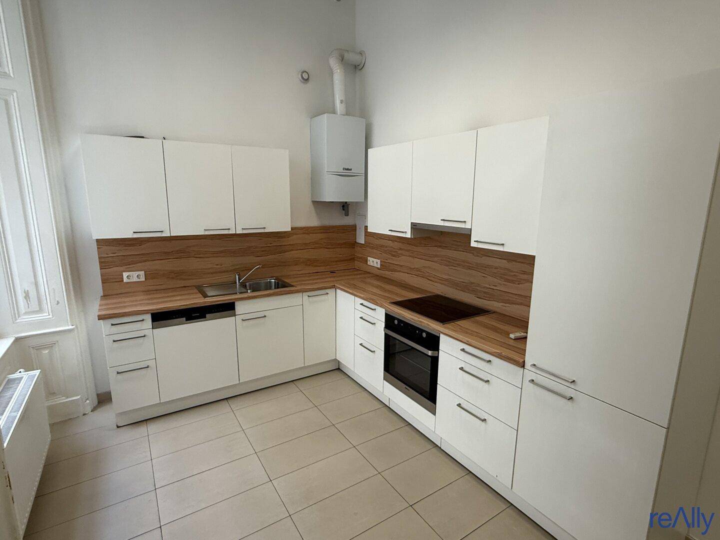 Moderne Einbauküche mit weißen Schränken, Holzarbeitsplatten und Fliesenboden.