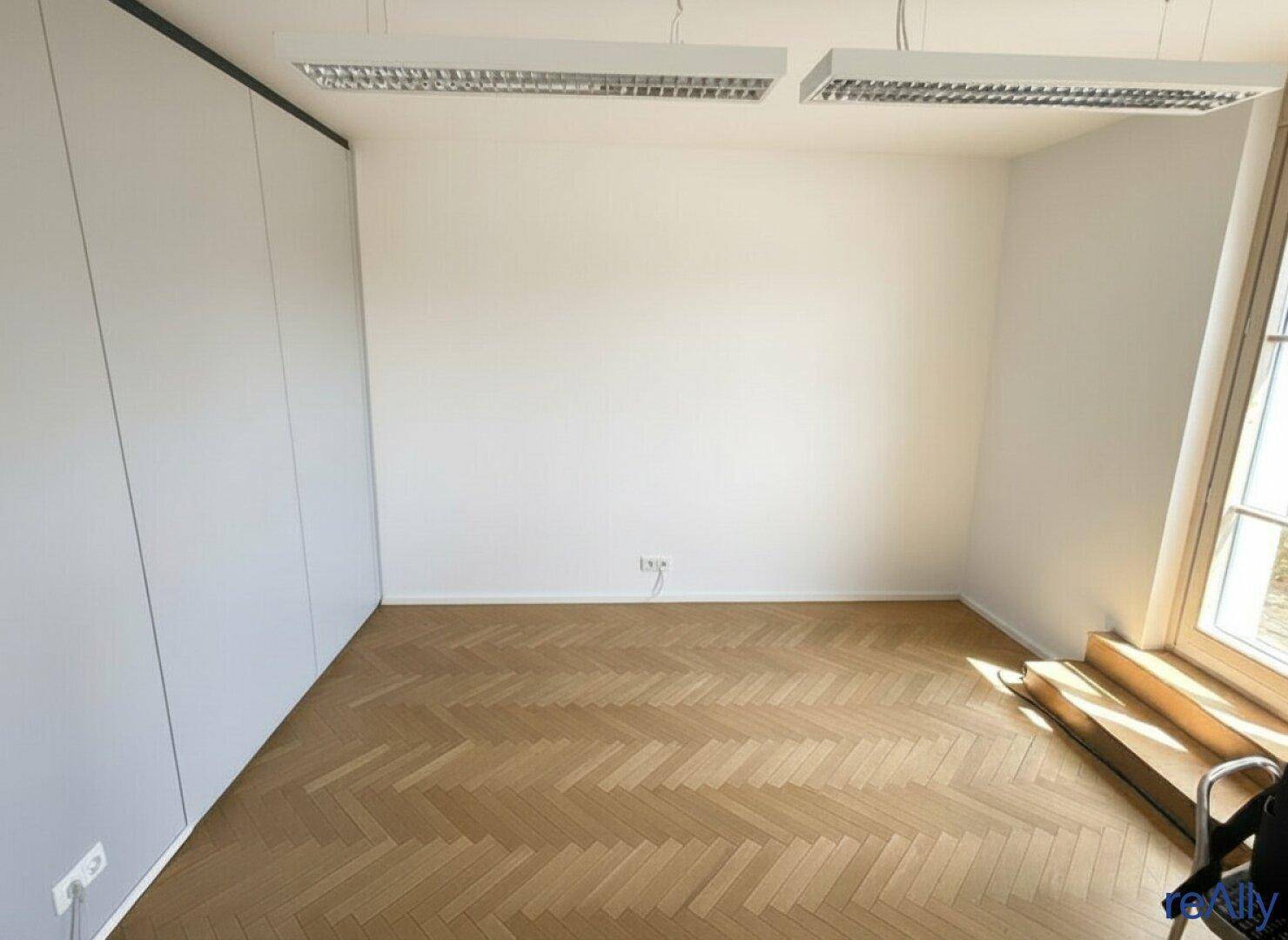 Heller Büroraum mit Fischgrätparkett und einer Wand aus Einbauschränken.
