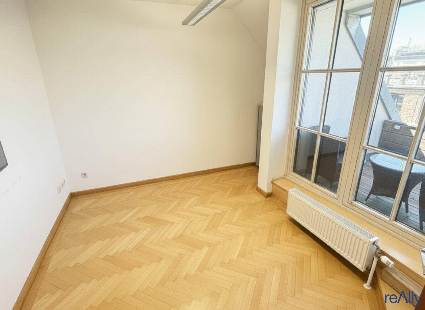 Heller Büroraum mit Fischgrätparkett und Zugang zu einem kleinen Balkon.
