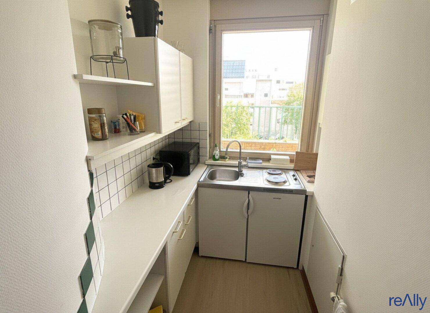 Kleine Küchenzeile mit Spüle, Kochfeld und Fenster, ideal für eine kompakte Nutzung.