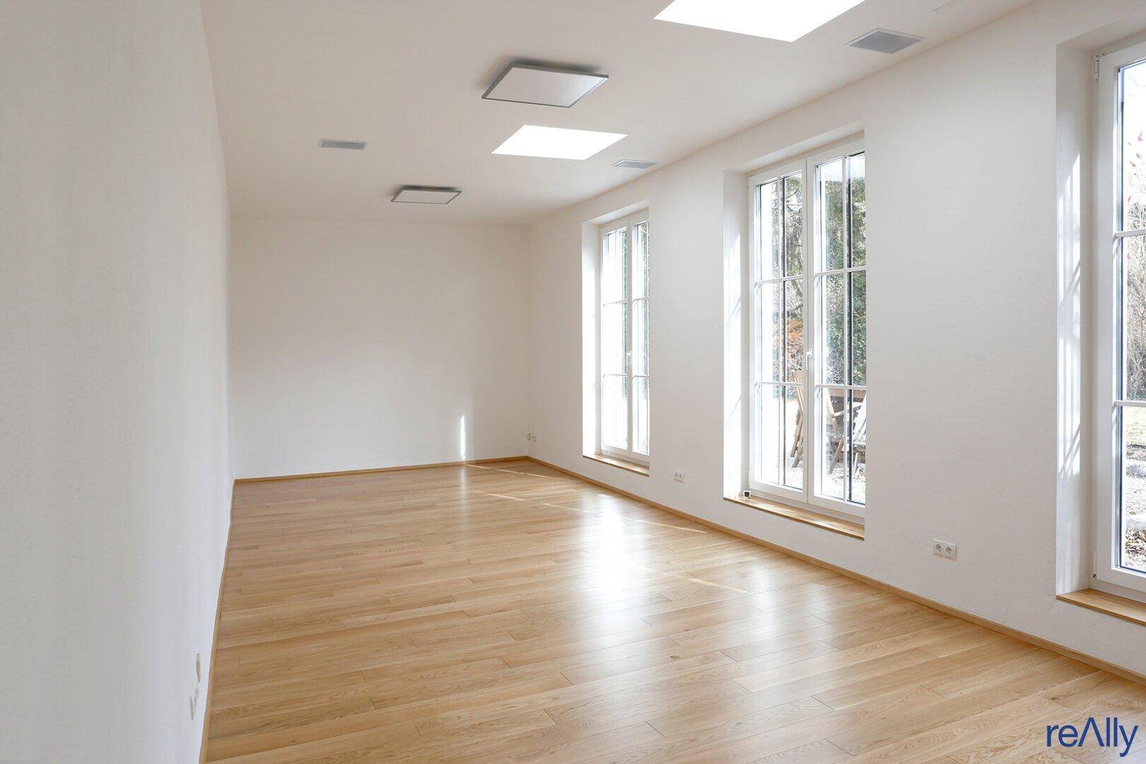 Lichtdurchfluteter Raum mit großen Fenstern und hellem Holzfußboden, ideal für Wohnzwecke.