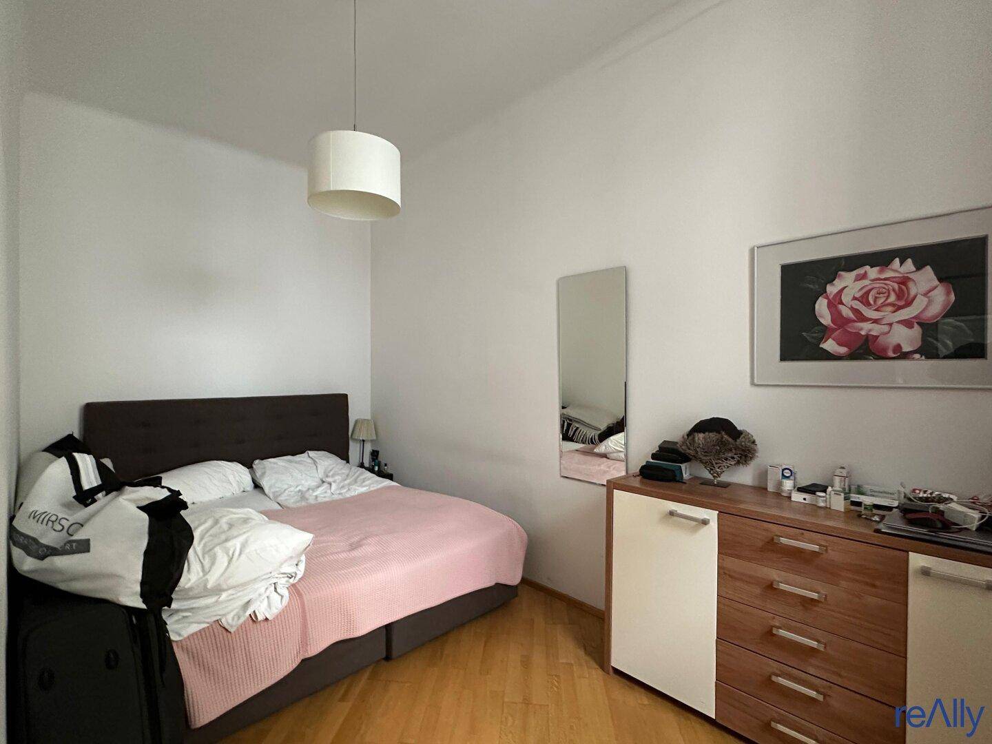 Helles Schlafzimmer mit Doppelbett, Holzboden und Kommode.
