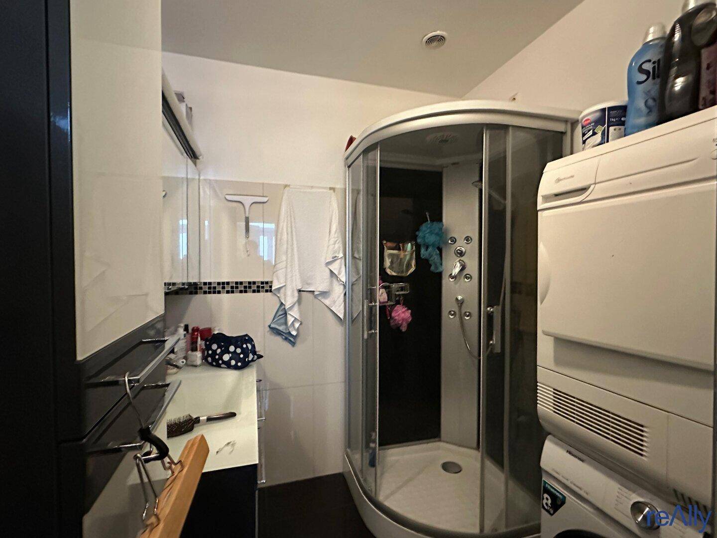 Badezimmer mit Duschkabine, Waschmaschine und Trockner.