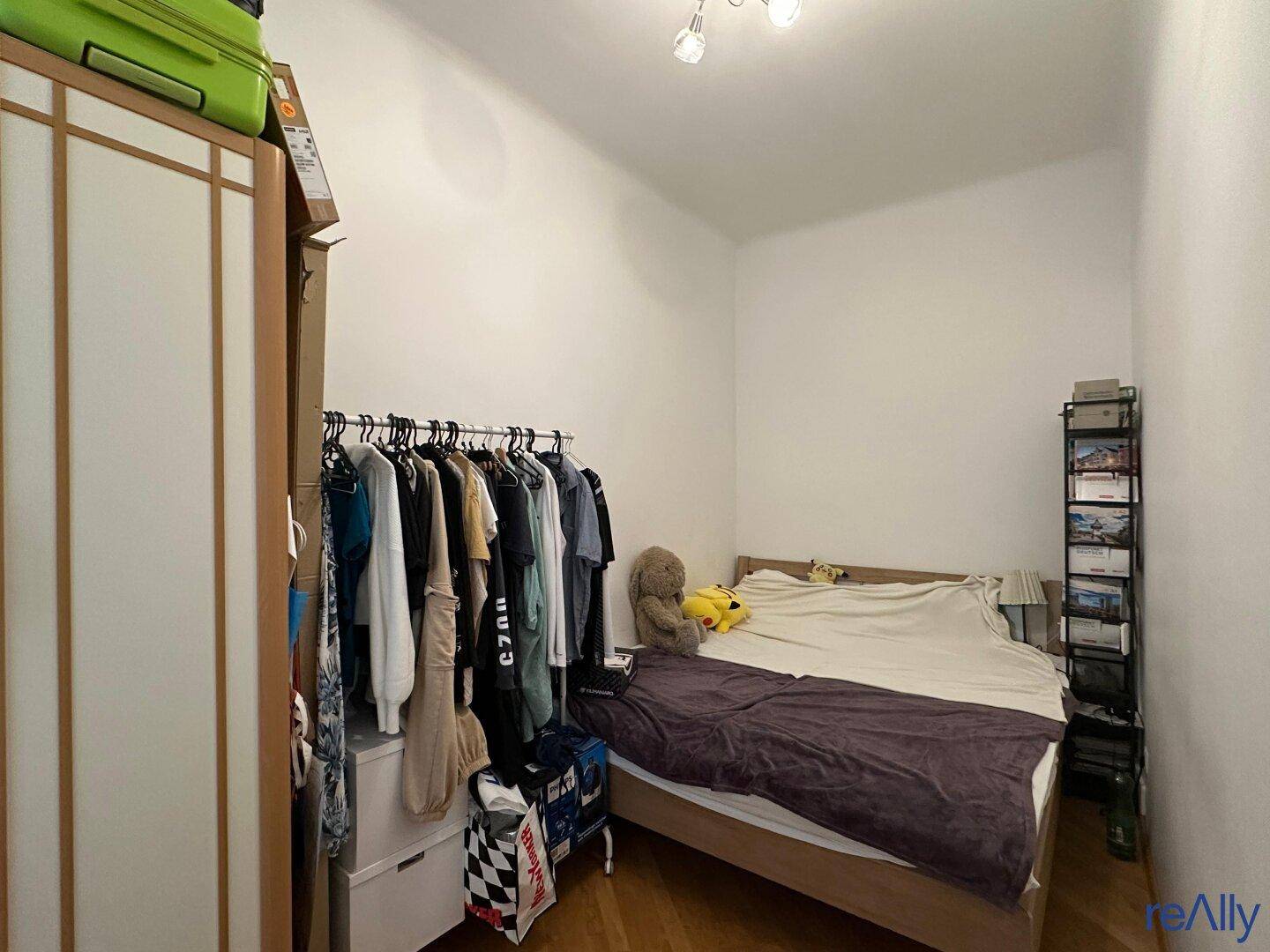 Schlafzimmer mit Holzboden, weiß gestrichenen Wänden und Kleiderstange.