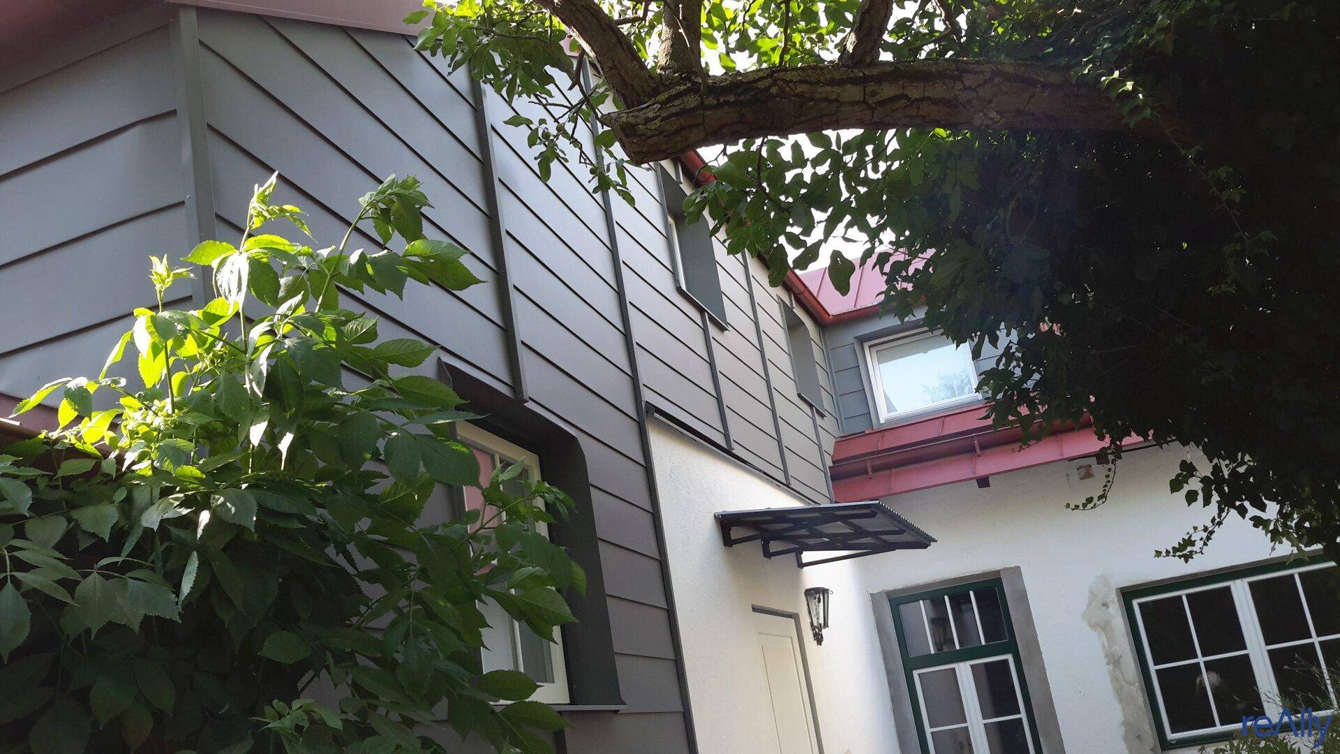 Detailansicht der Hausfassade mit moderner Verkleidung und traditionellen Fenstern.