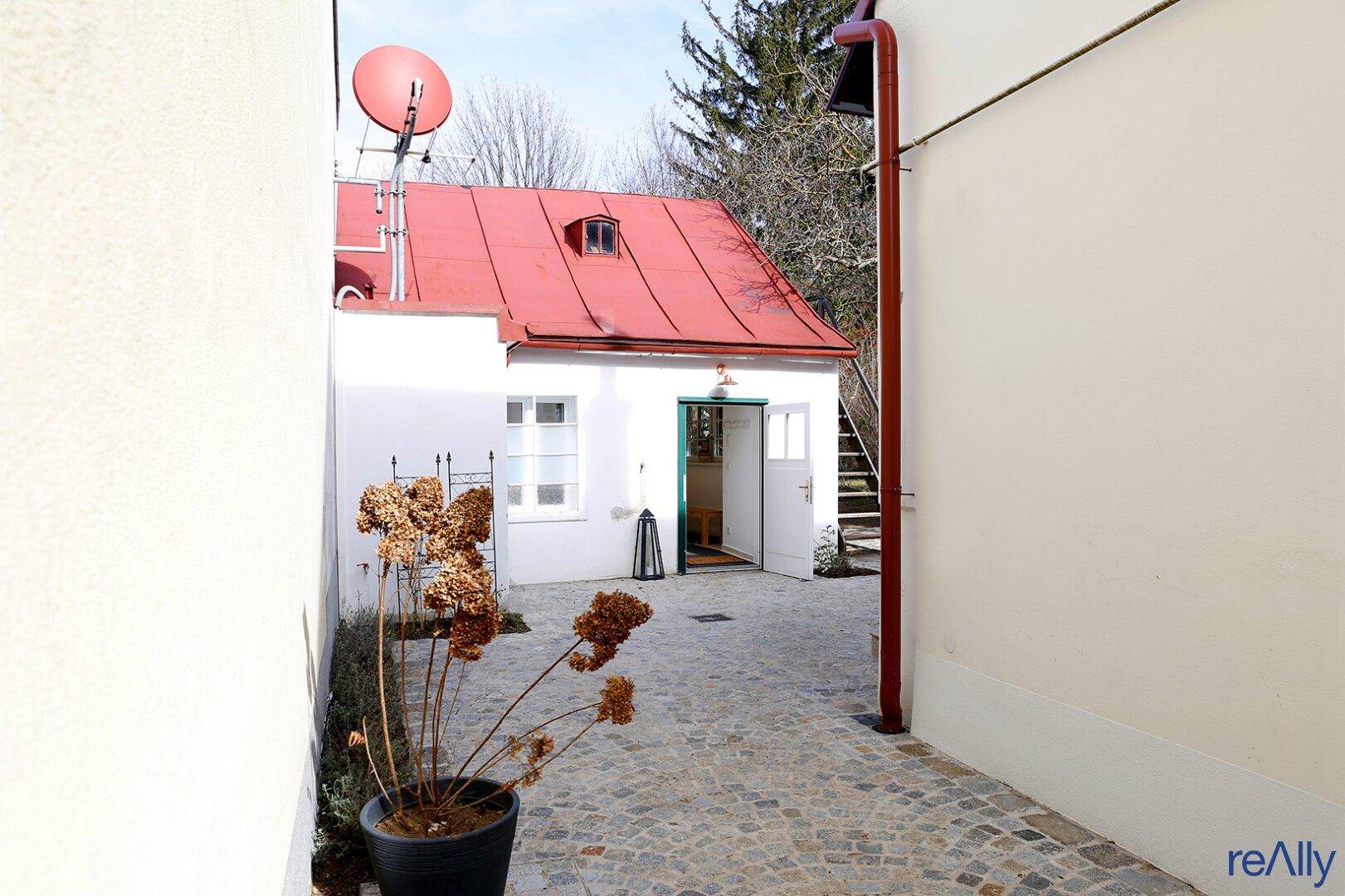 Kopfsteinpflasterweg führt zum Eingang eines Hauses mit rotem Dach und Satellitenschüssel.
