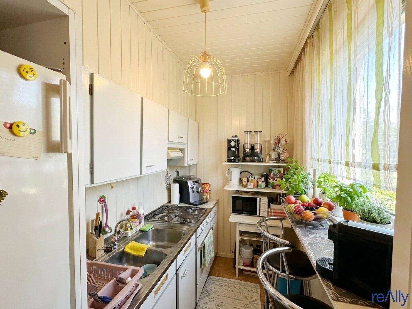 Kleine Küche mit weißen Schränken, Holzvertäfelung und einem Fenster über der Spüle.