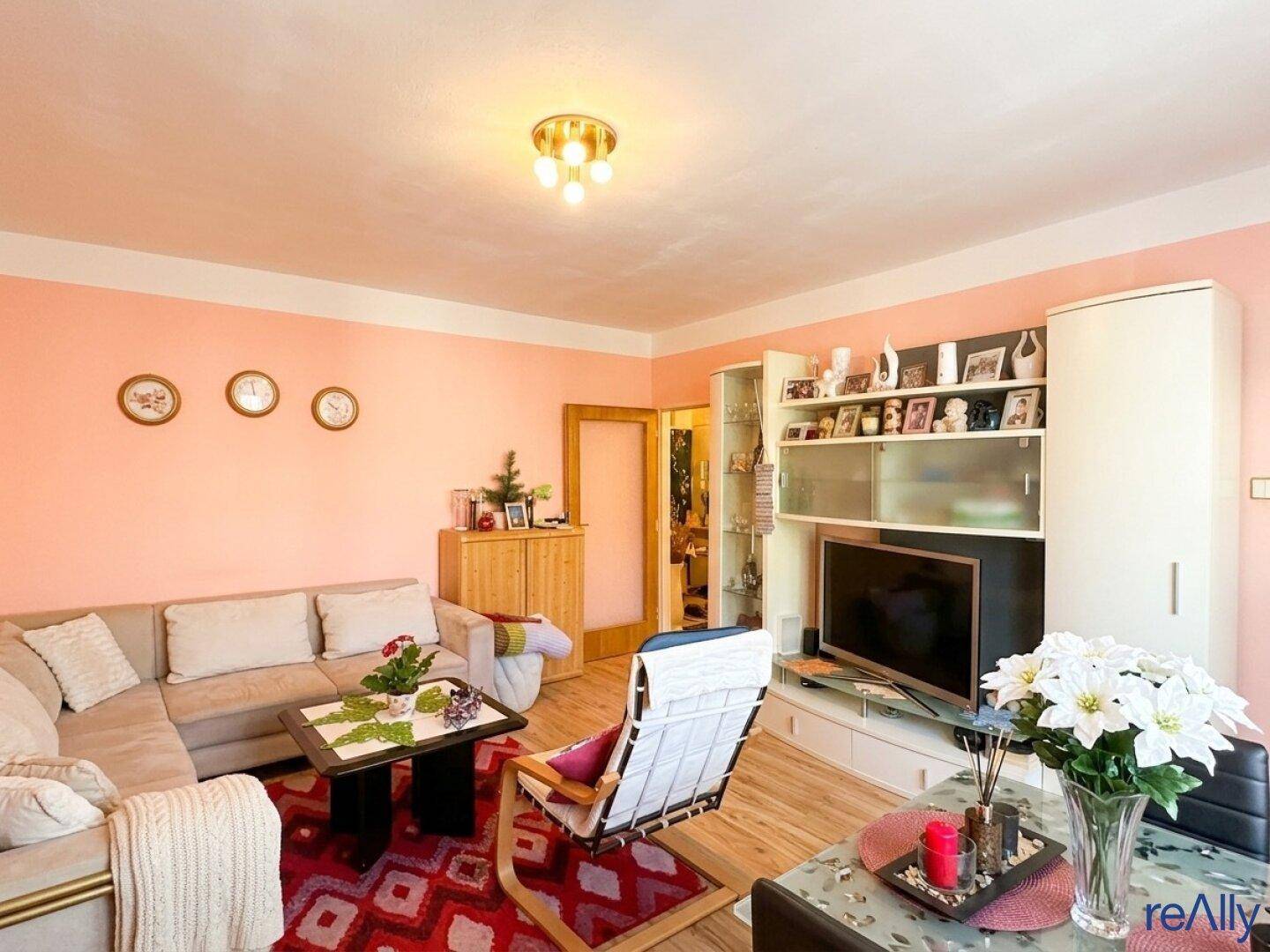 Helles Wohnzimmer mit beiger Couch, Holzmöbeln und einem Medienelement an der Wand.