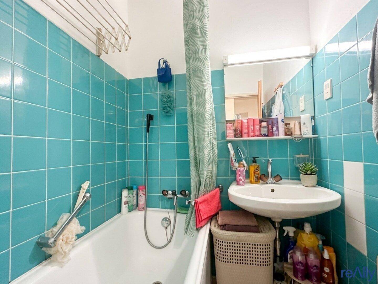 Badezimmer mit türkisfarbenen Fliesen, Badewanne mit Duschfunktion und einem Waschbecken.