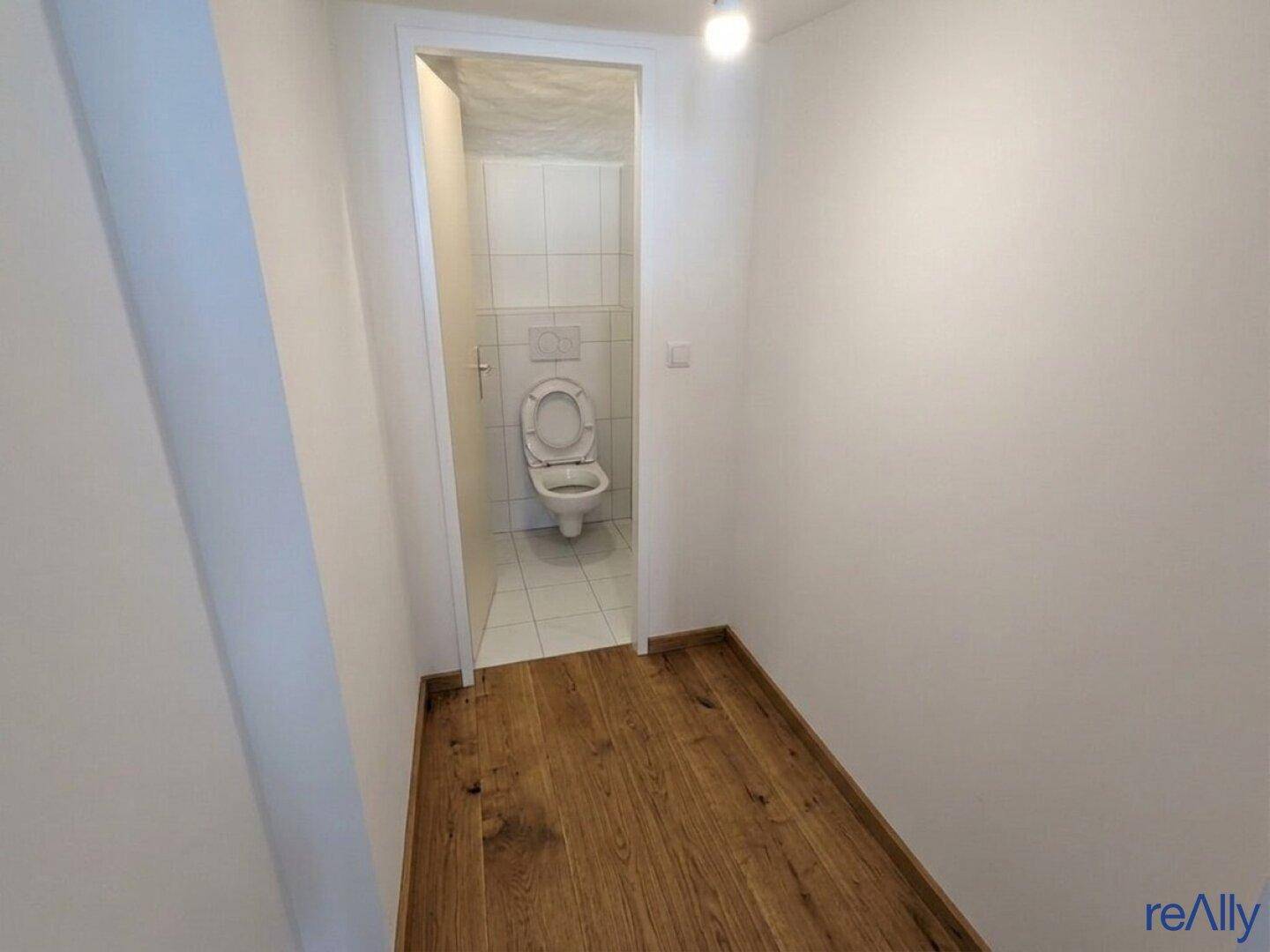 Kleiner Flur führt zu einer Toilette mit weißen Fliesen und einem Wand-WC.