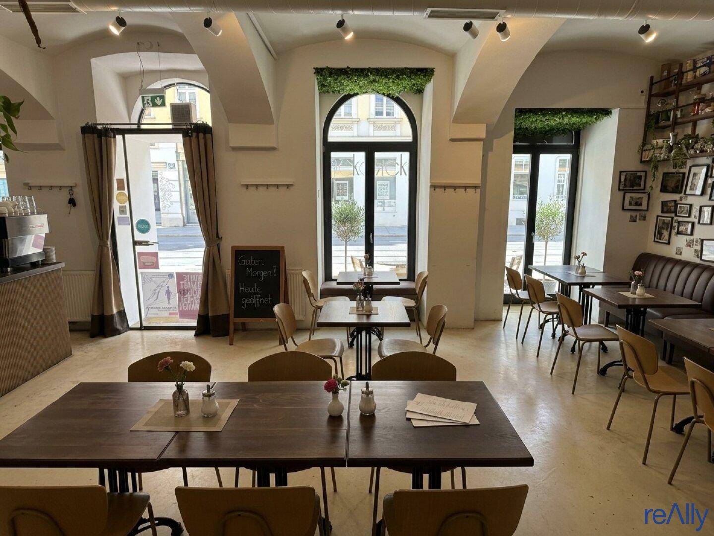 Heller Restaurantbereich mit großen Bogenfenstern, Holztischen und modernen Stühlen, die zum Verweilen einladen.
