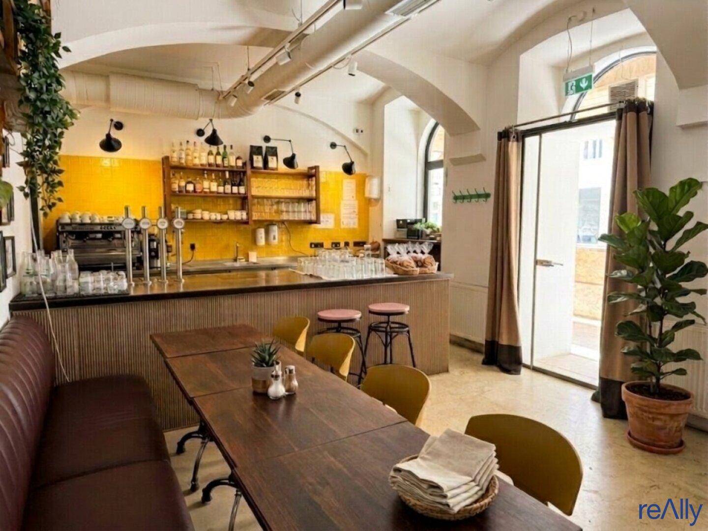 Lebhafter Restaurantbereich mit gelben Fliesenwänden hinter der Theke und weiteren Sitzgelegenheiten für Gäste.