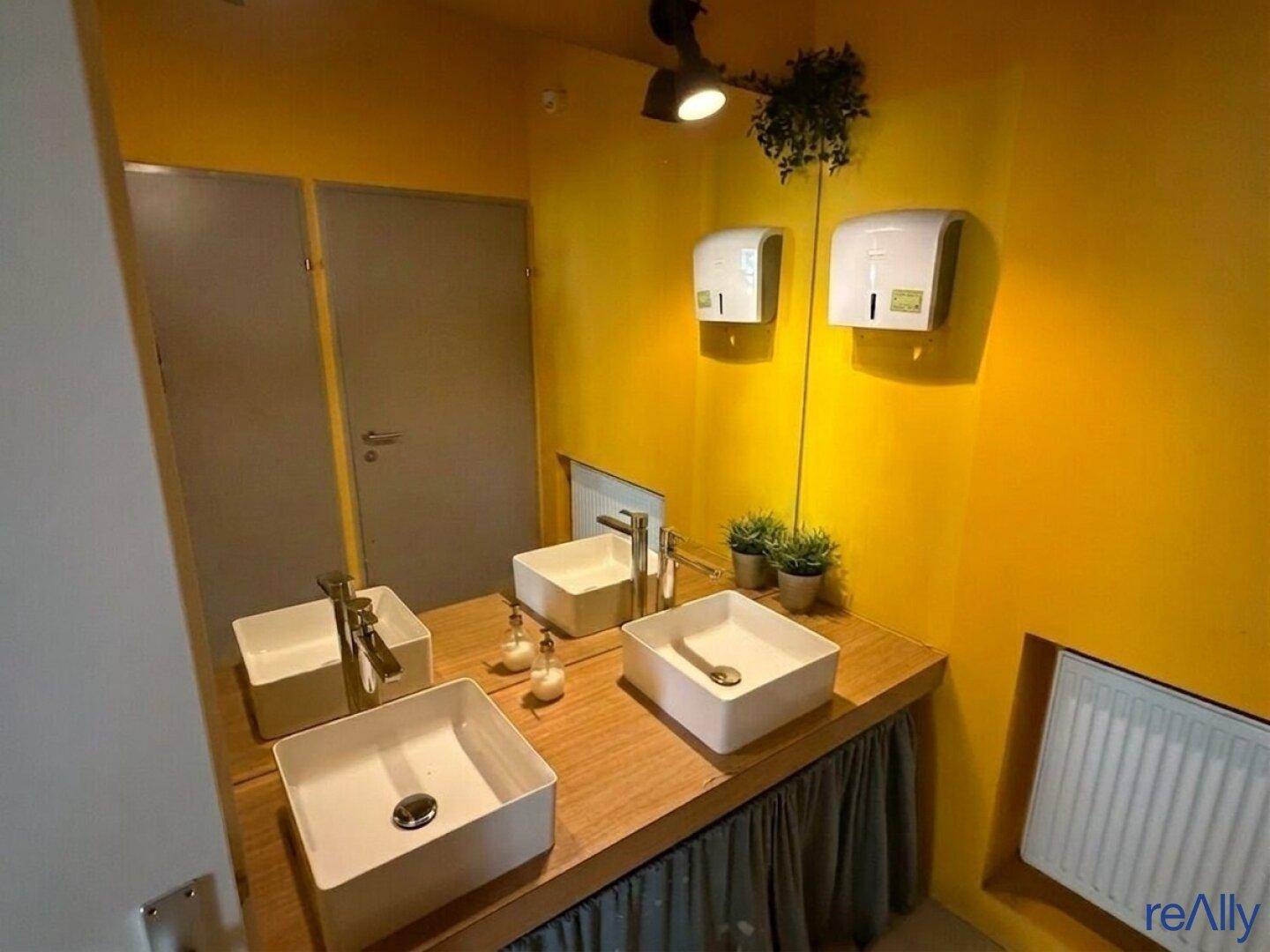Moderner öffentlicher Waschraum mit mehreren Aufsatzwaschbecken, gelben Wänden und Handtuchspendern.