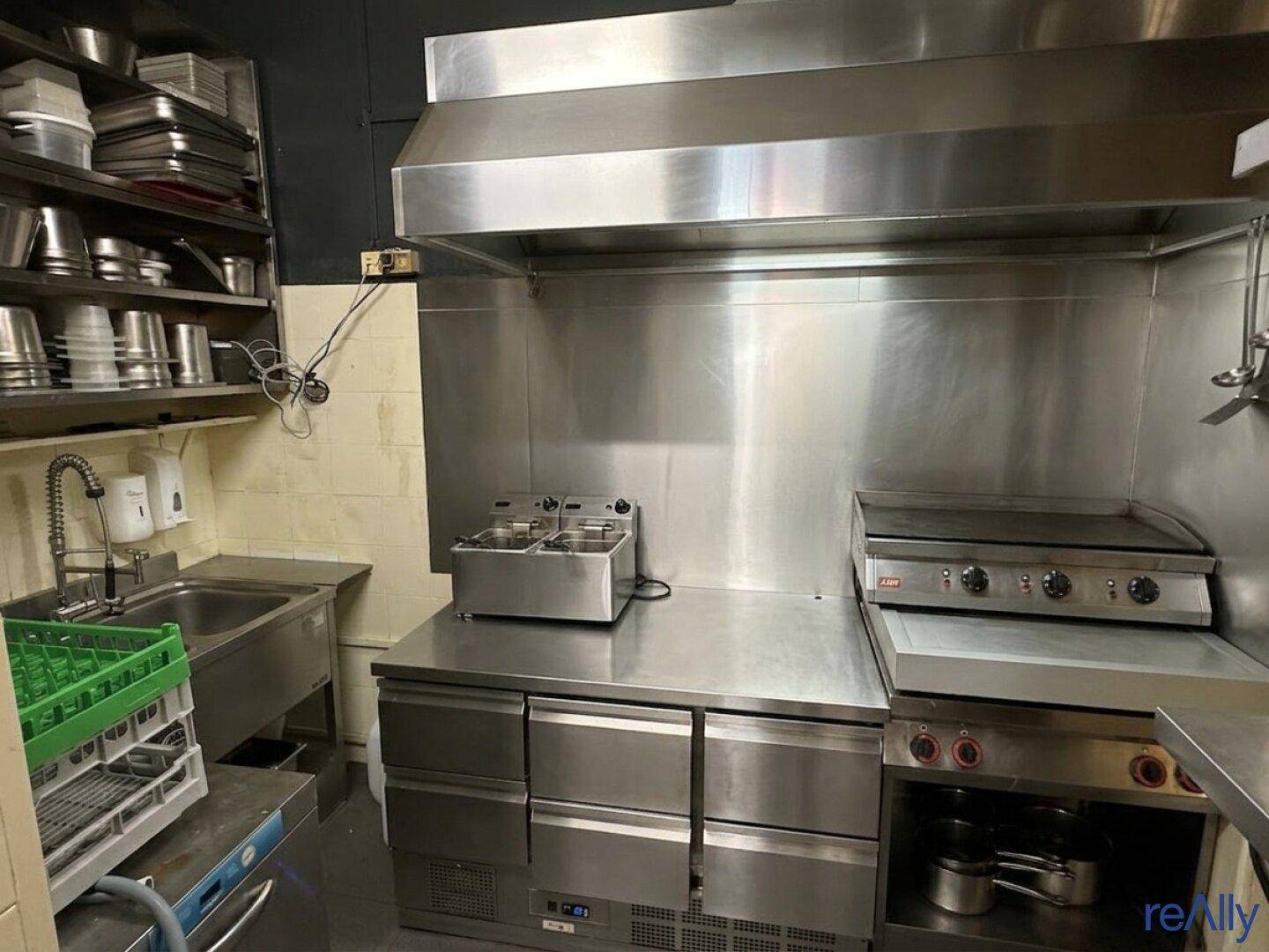 Professionelle Gewerbeküche mit Edelstahlgeräten, Dunstabzugshaube und Fritteuse für den Restaurantbetrieb.