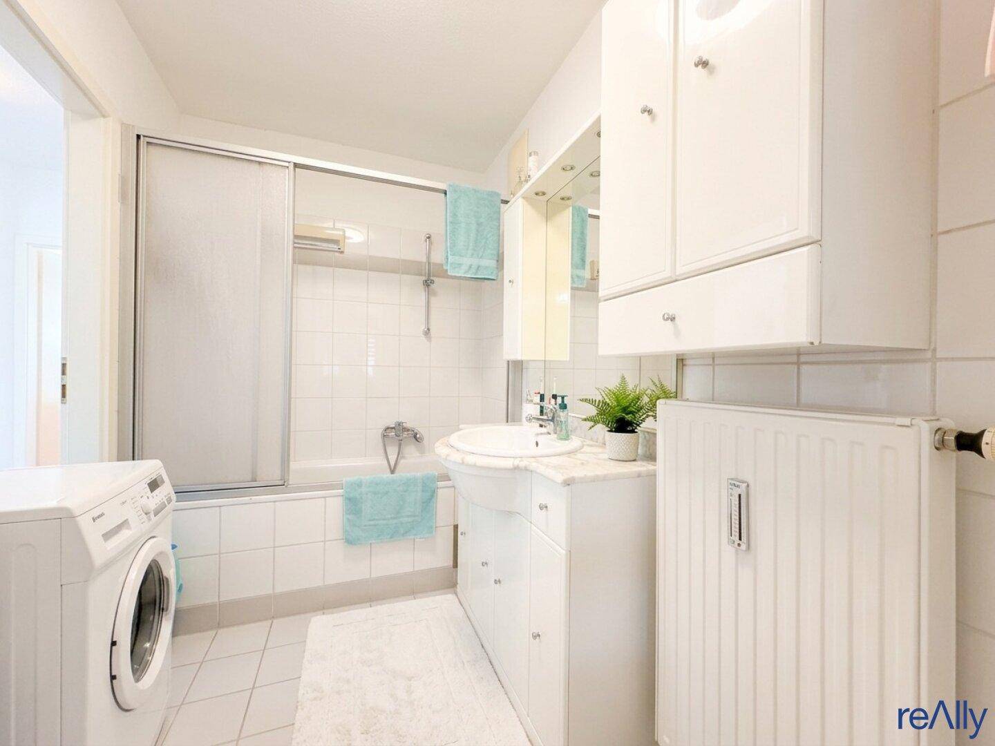Helles Badezimmer mit Badewanne, Duschvorrichtung, Waschbecken und Waschmaschine.