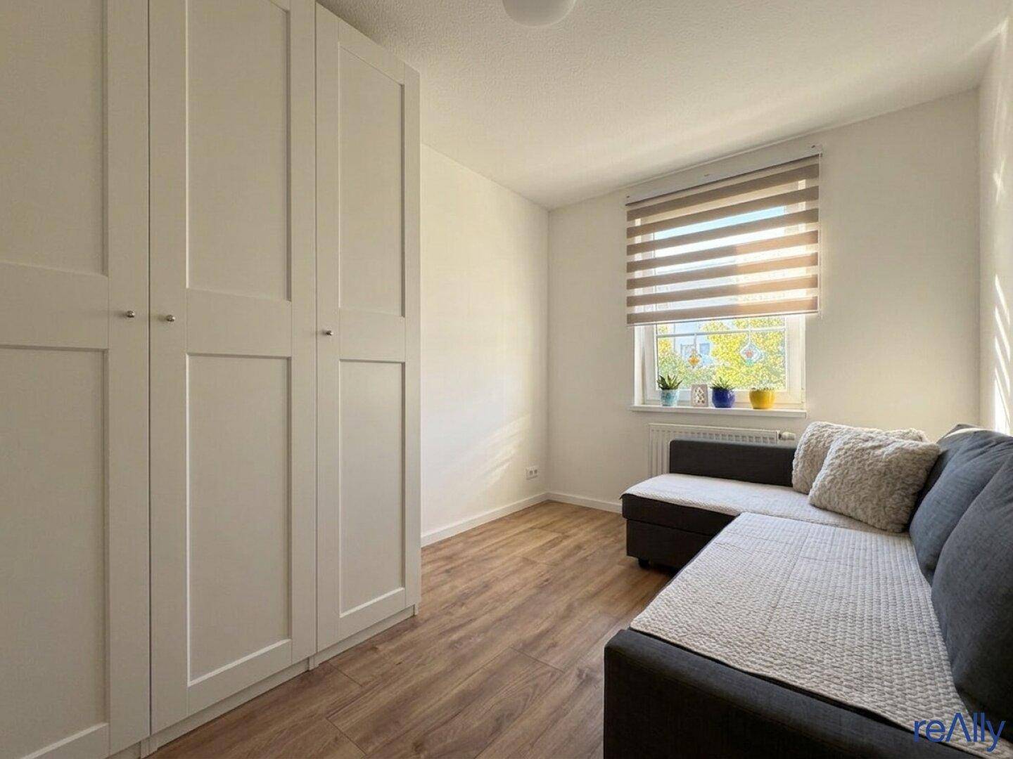 Helles Zimmer mit großem Kleiderschrank, Sofa und Holzfußboden.