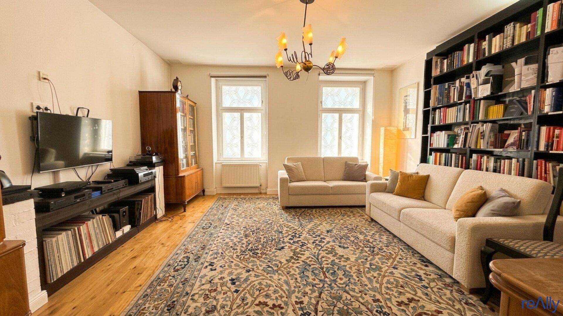 Geräumiges Wohnzimmer mit Bücherregal, zwei Sofas und traditionellem Teppich.