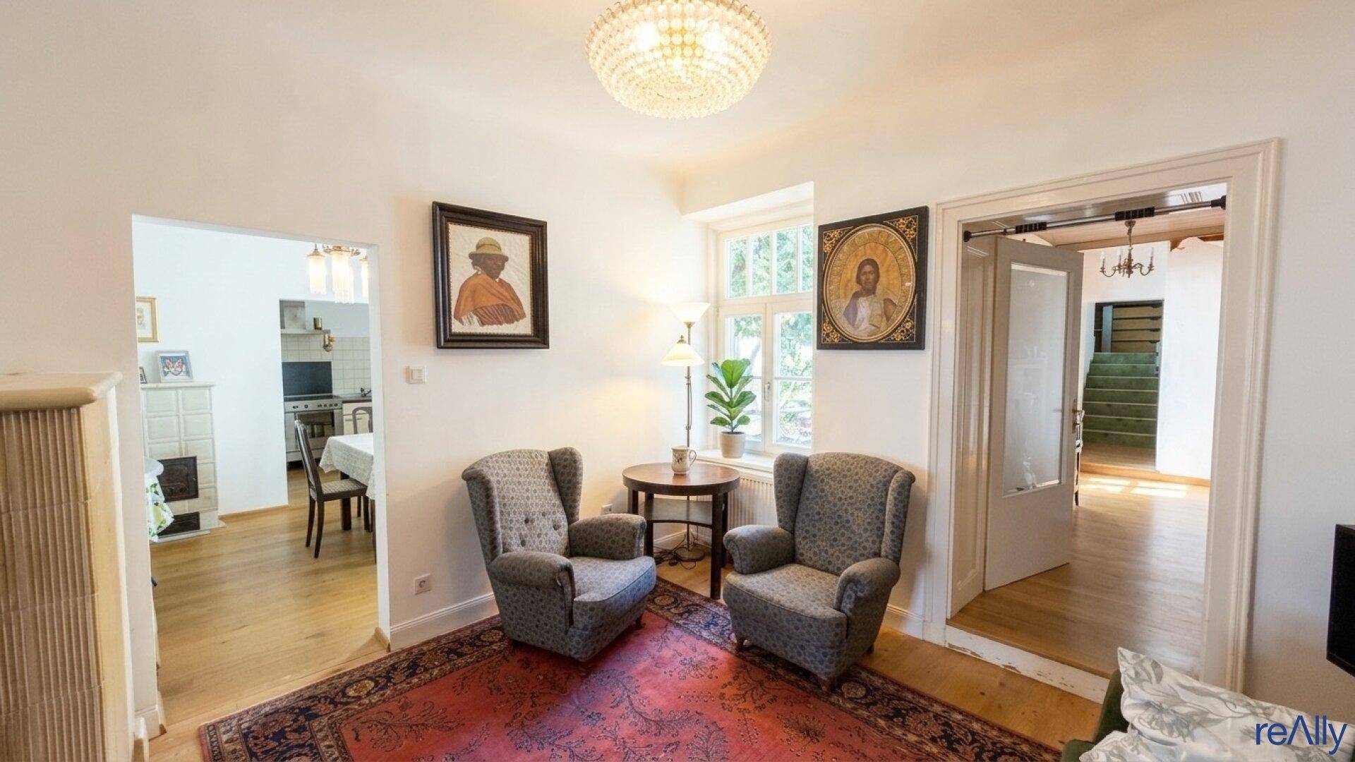 Traditionell eingerichtetes Wohnzimmer mit Teppich, Ohrensesseln und Kronleuchter.