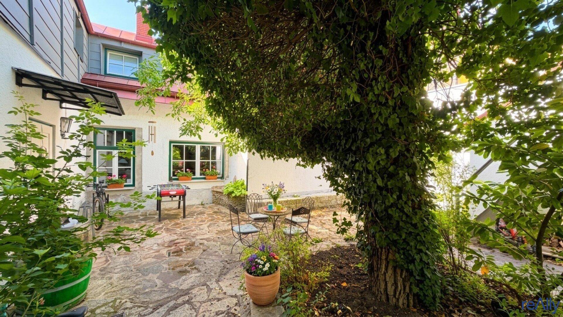 Gemütlicher Innenhof mit Sitzgelegenheiten, üppiger Begrünung und Kletterpflanzen am Baum.