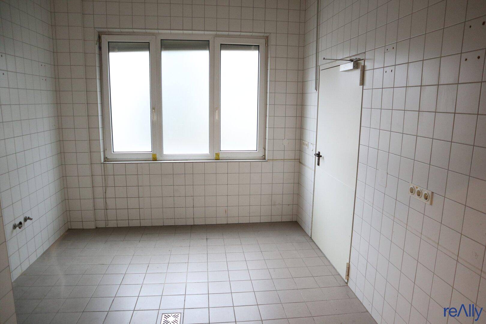 Einfacher Raum mit weißen Fliesen an Wänden und Boden sowie einem Fenster.
