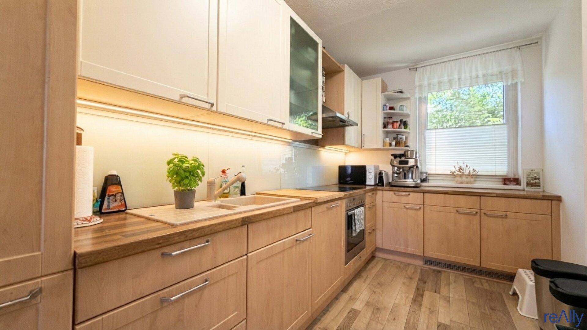 Funktionale Küche mit hellen Holzfronten, Arbeitsplatte und Fenster für Tageslicht.