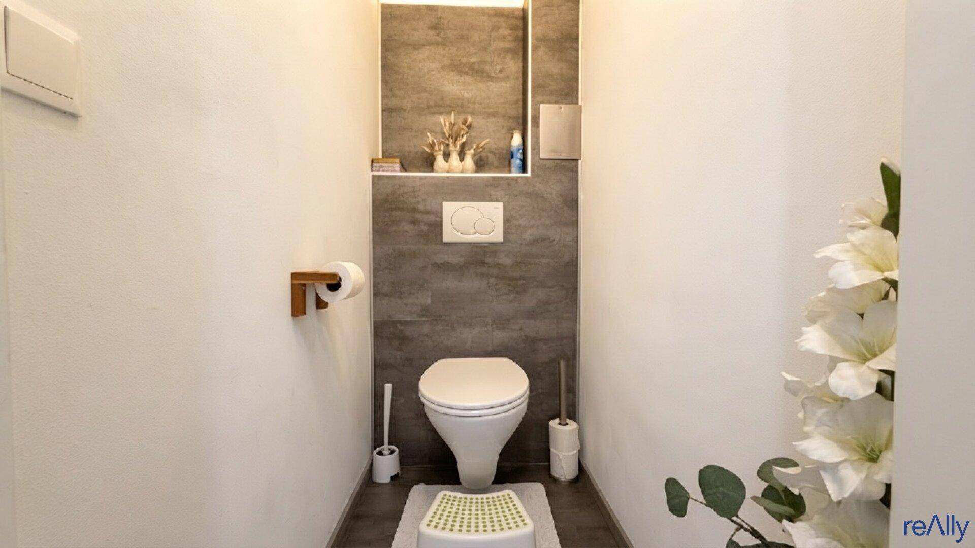 Modernes Gäste-WC mit Wand-WC und dunklen Fliesenakzenten an der Wand.
