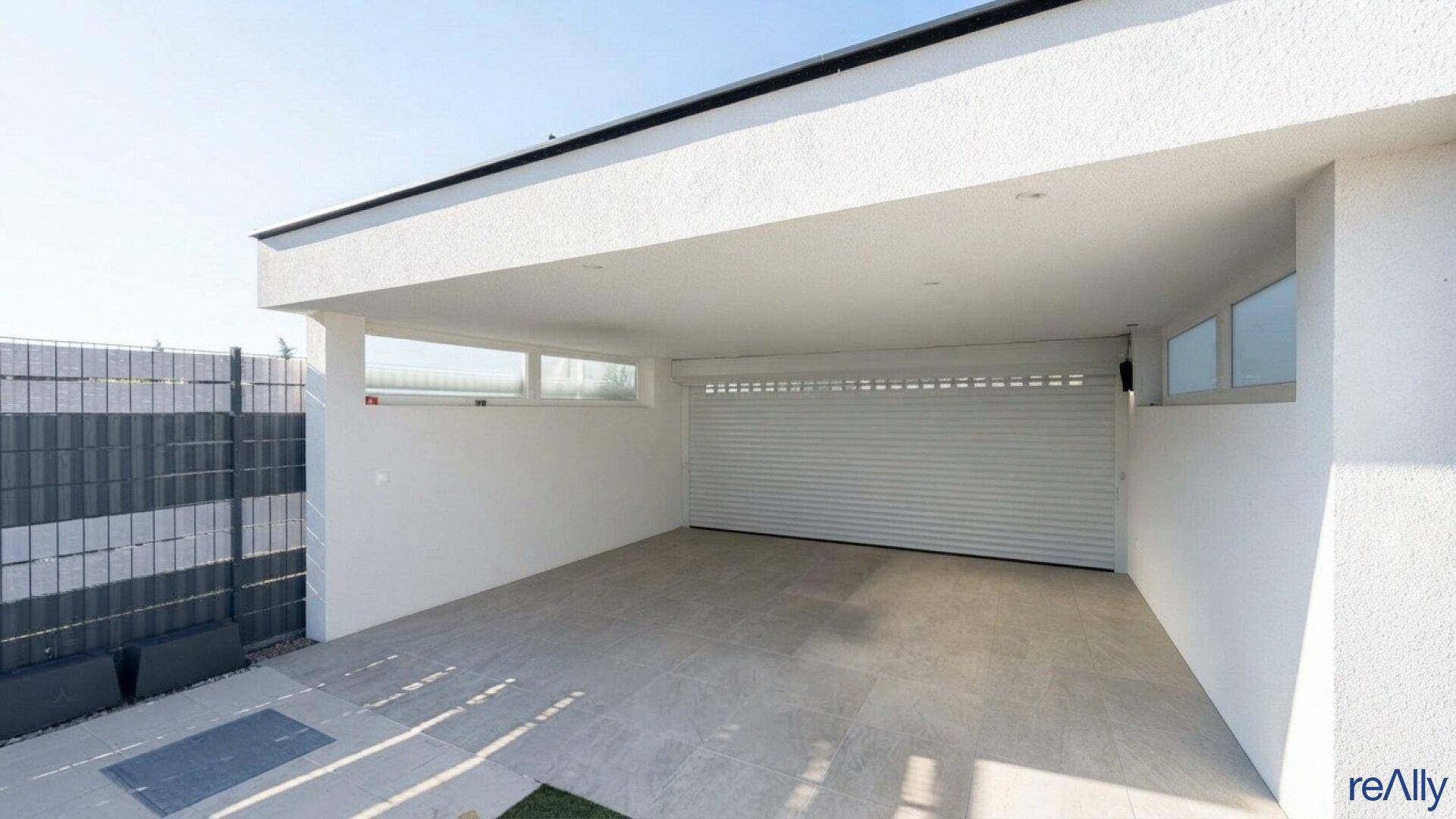 Überdachter Stellplatz und Garage mit Rolltor und gepflastertem Bereich.
