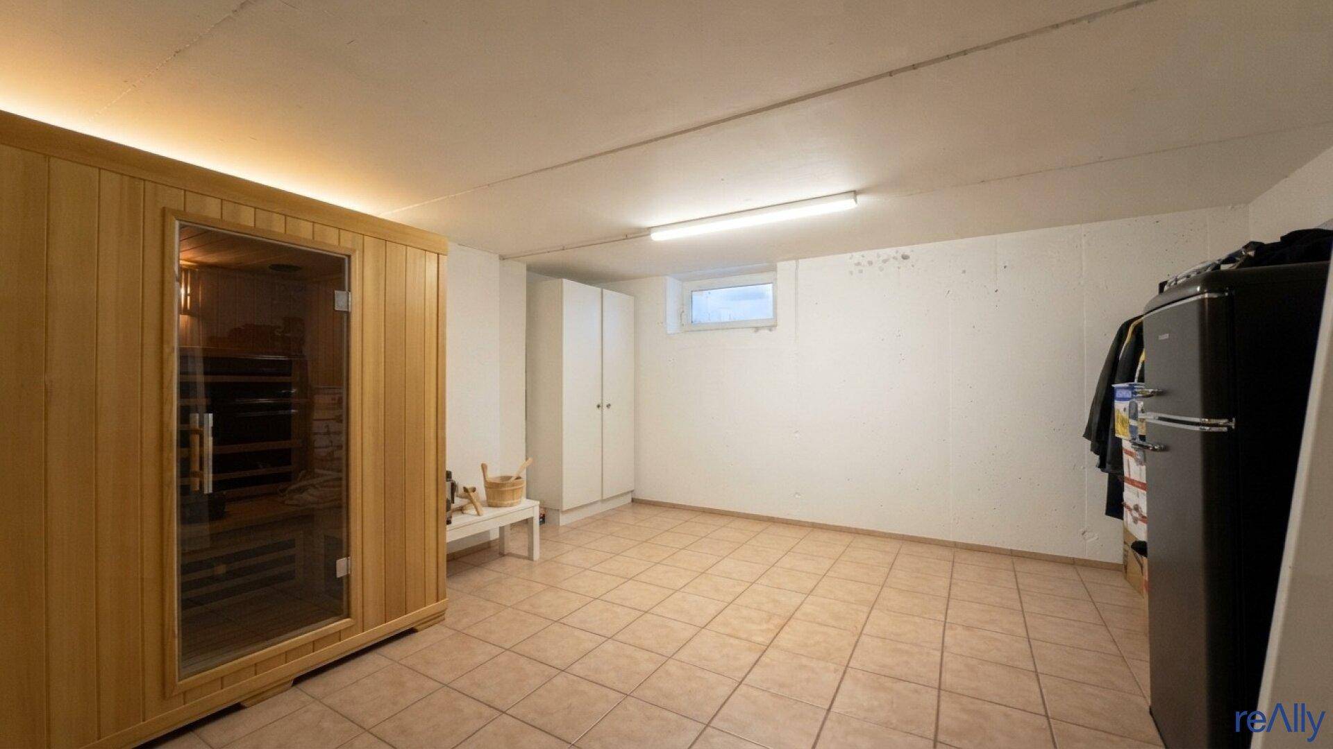 Geräumiger Kellerraum mit integrierter Sauna, Fliesenboden und kleinem Fenster.