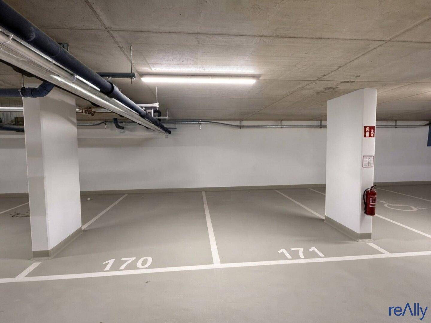 Tiefgarage mit markierten Stellplätzen und sichtbaren Versorgungsleitungen an der Decke.