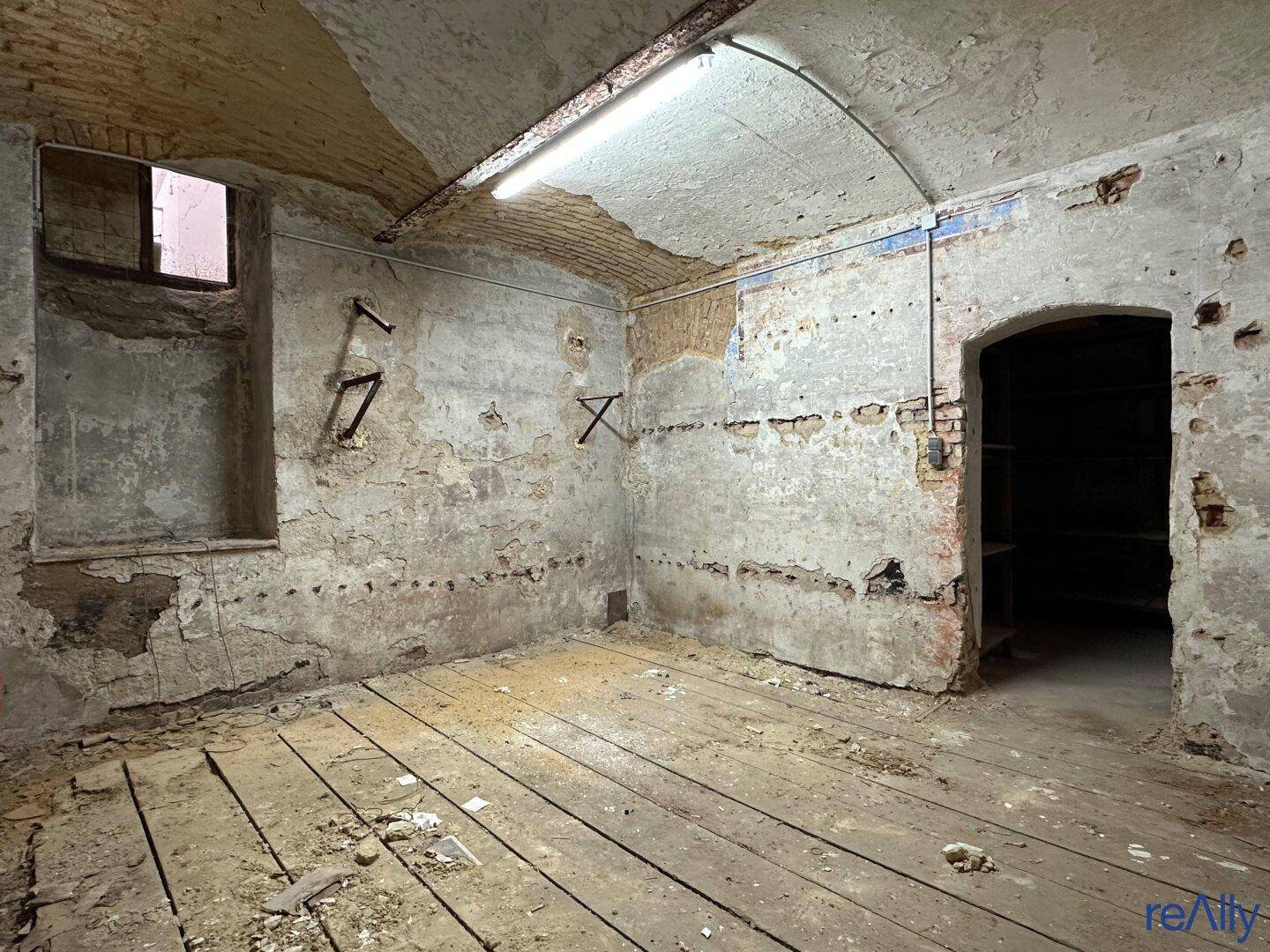 Kellerraum mit Holzdielenboden, unverputzten Wänden und einem kleinen Fenster, der auf eine Modernisierung wartet.