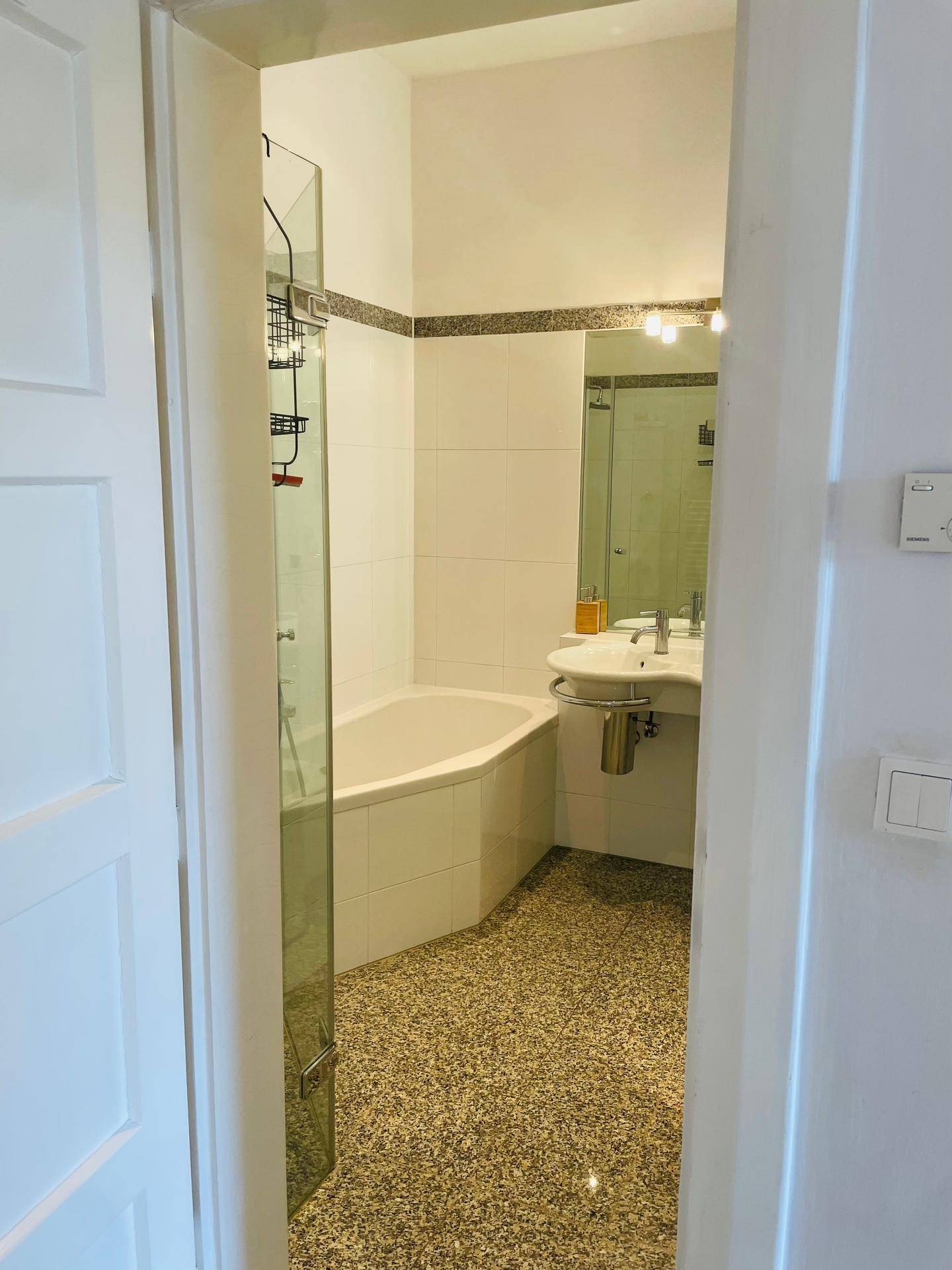Badezimmer mit Eckbadewanne, Duschabtrennung, Waschbecken und großem Spiegel.