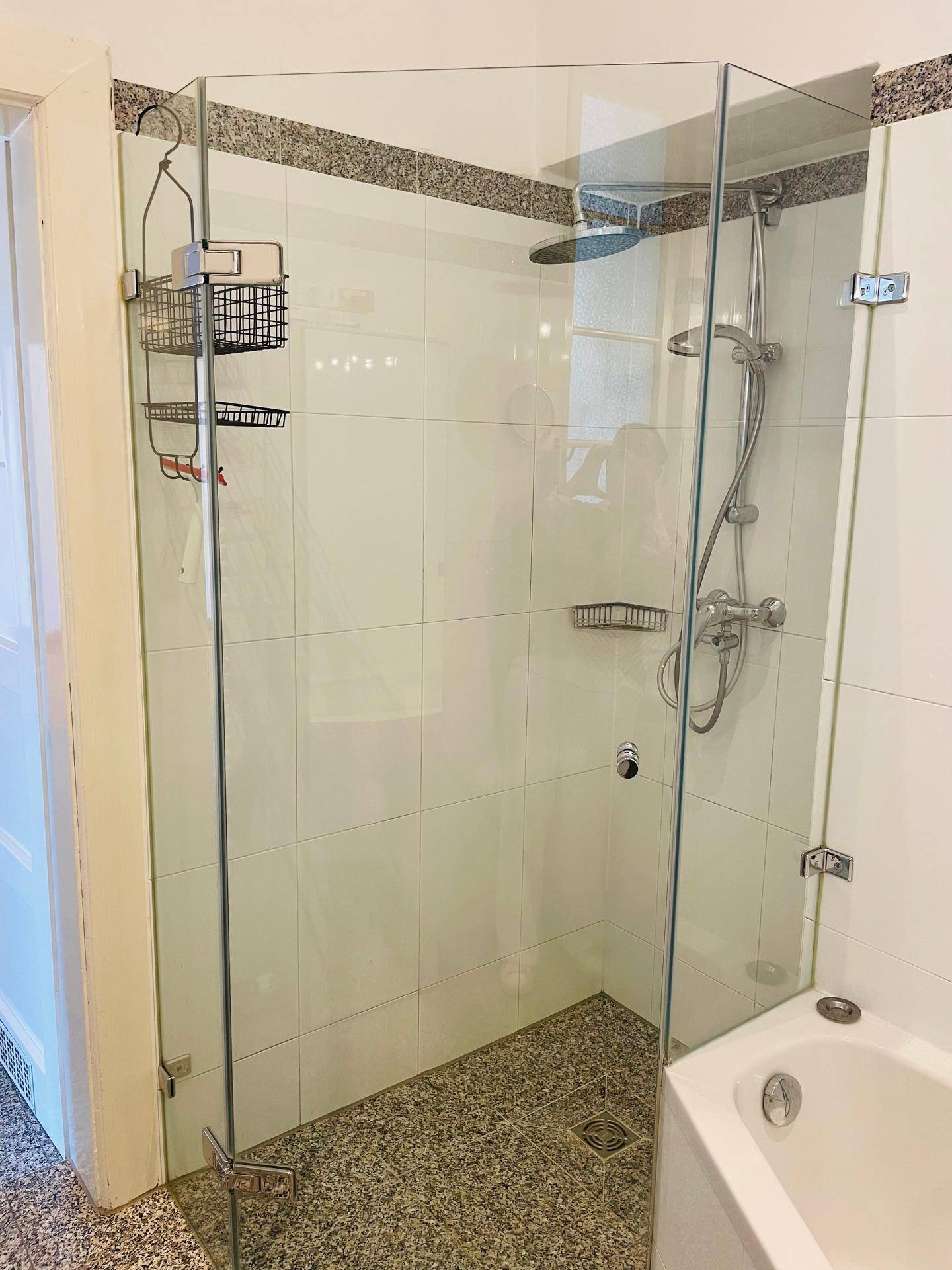 Duschbereich mit Glasabtrennung und Fliesenboden, direkt neben der Badewanne.