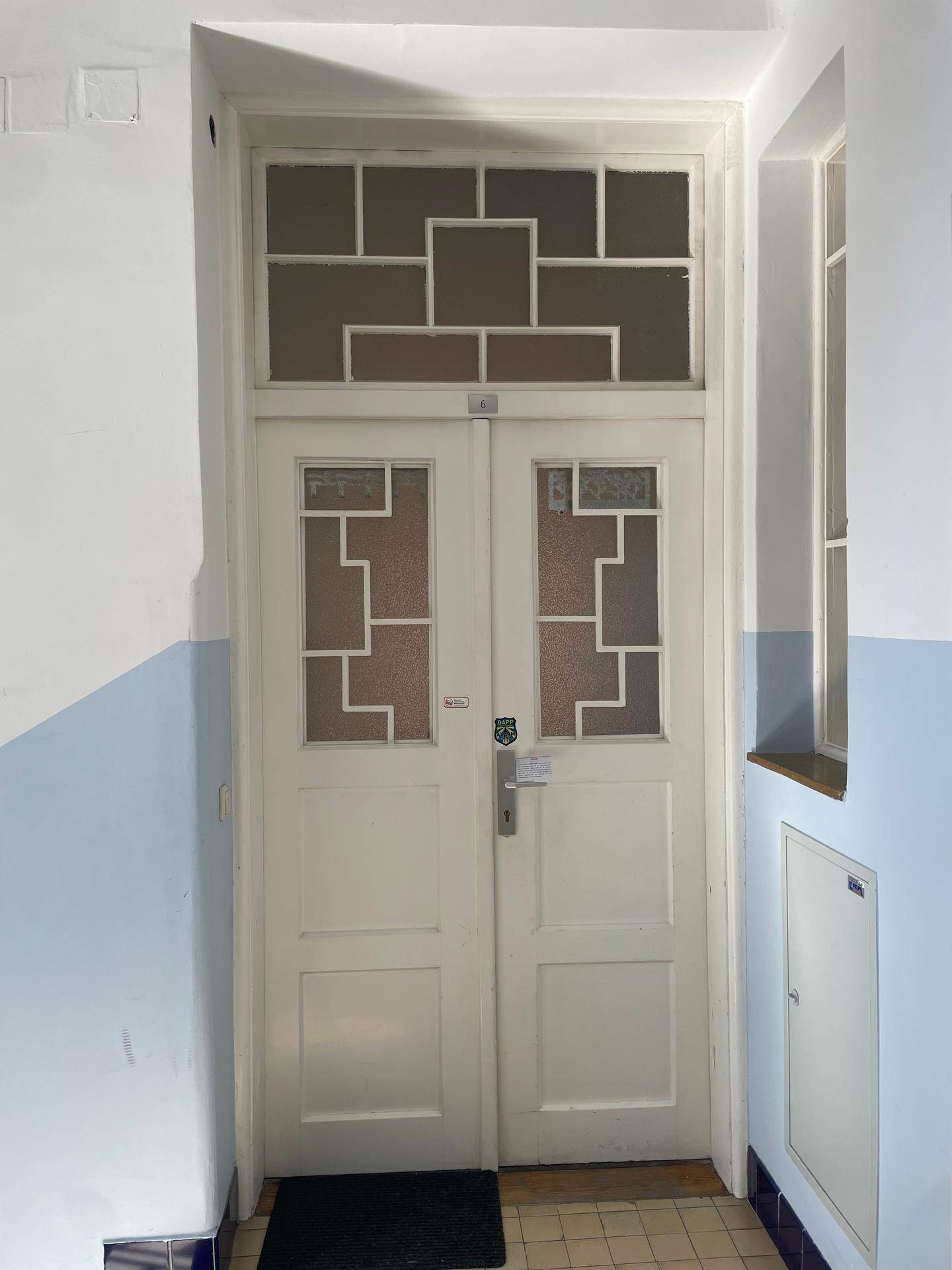 Eingangstür mit dekorativen Glasausschnitten in einem hellen Treppenhausbereich.