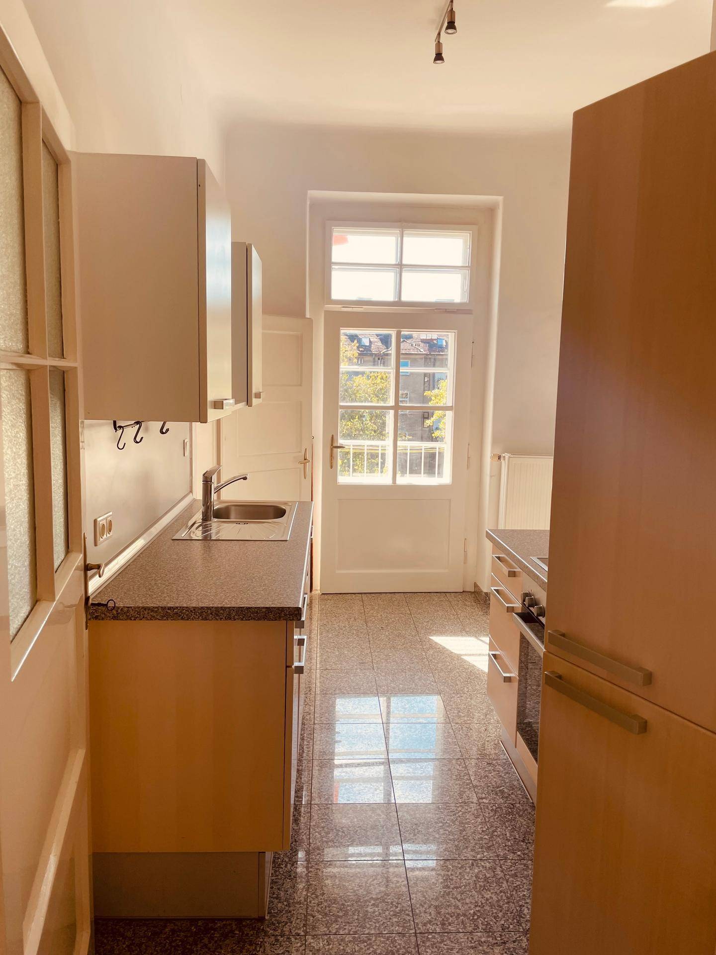Helle Küche mit funktionalen Einbauschränken, Granit-Arbeitsplatte und Zugang zum Balkon.