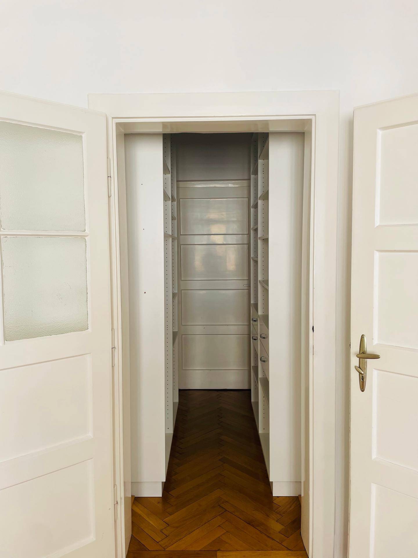 Eingangsbereich zu einem begehbaren Kleiderschrank mit offenen Türen und Regalsystemen.