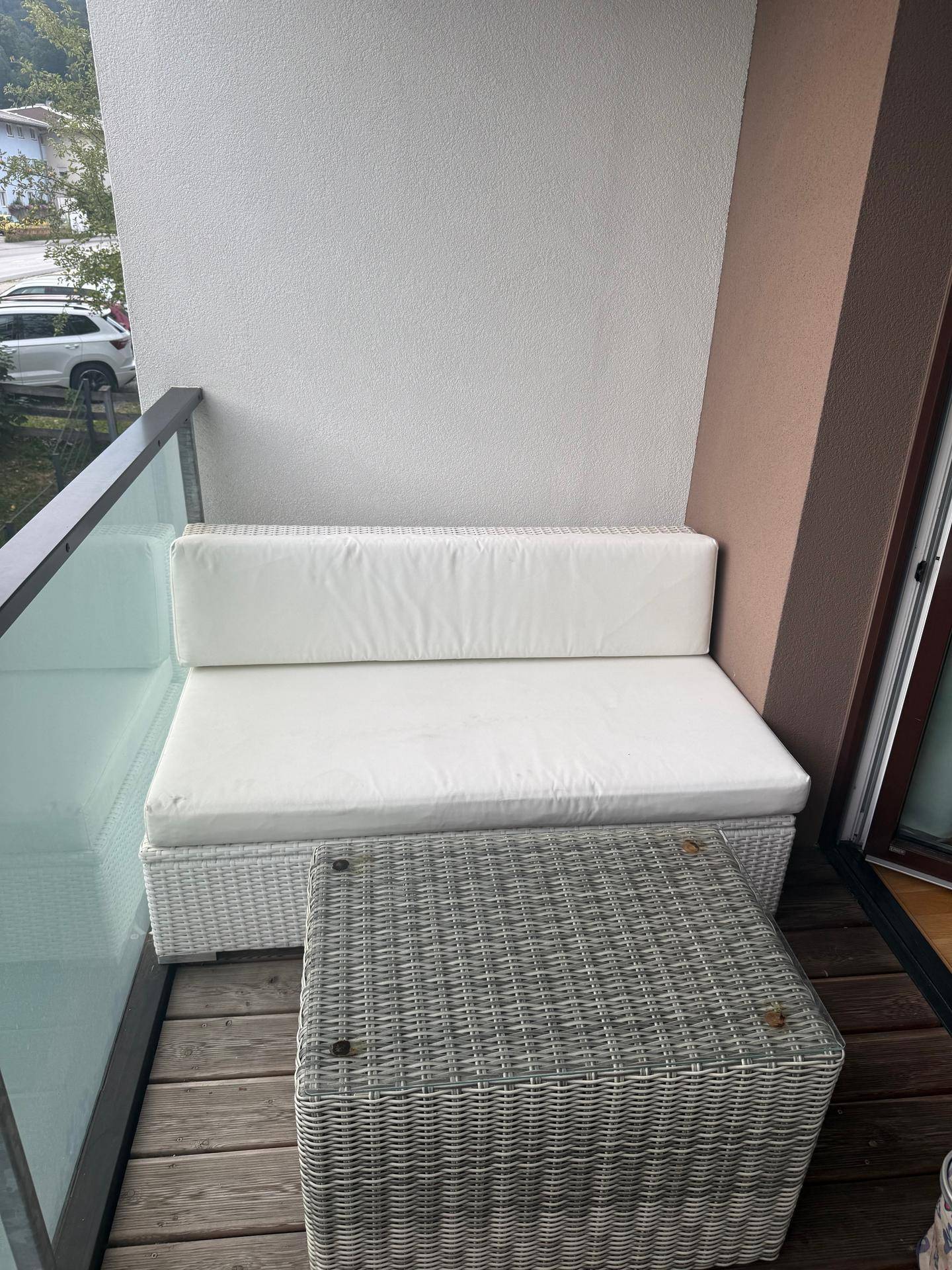 Kleiner Balkon mit Rattan-Sitzmöbeln und Blick auf die Umgebung.