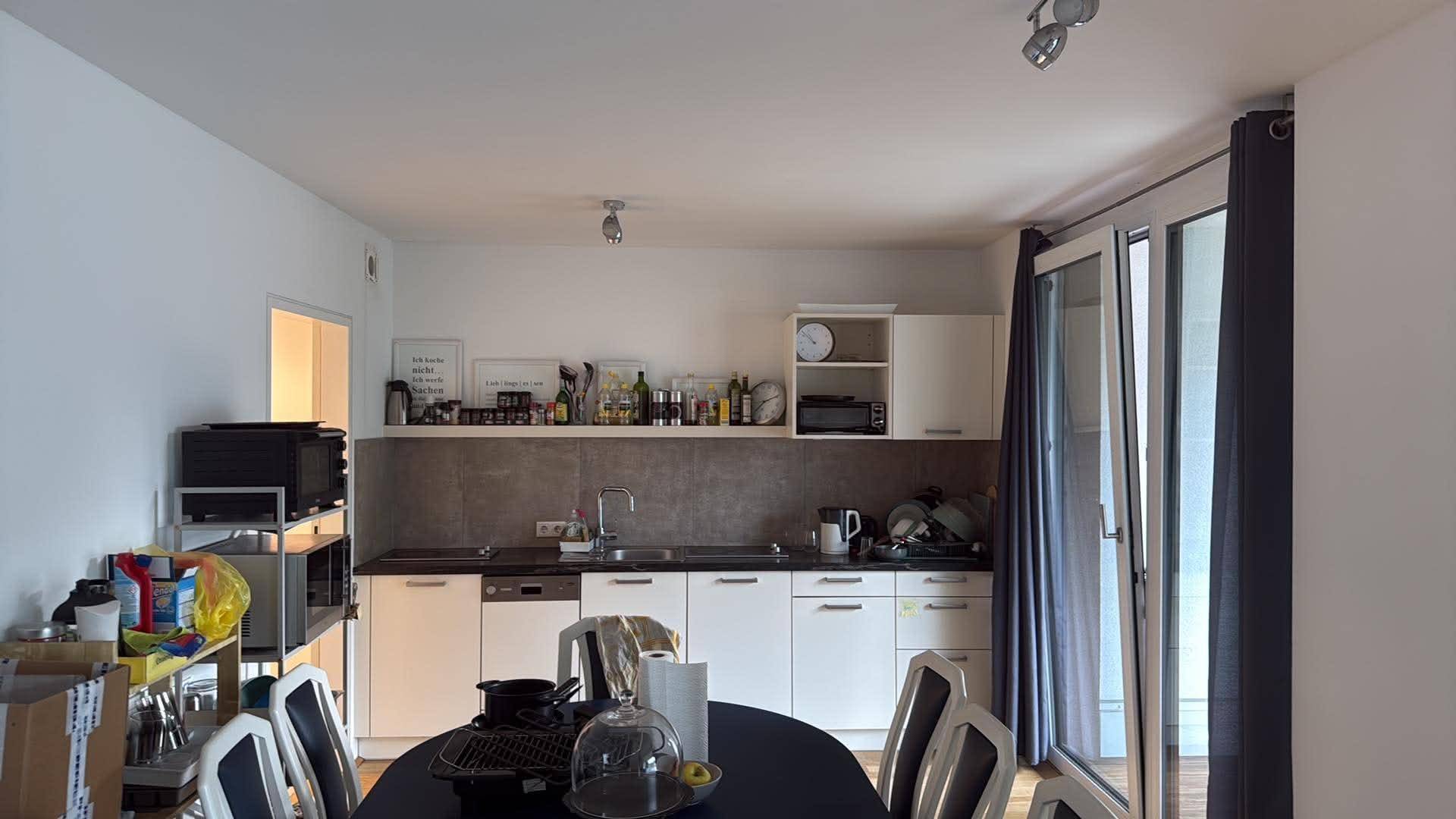 Küche mit Essbereich, Einbauschränken und Zugang zum Balkon durch eine Glastür.