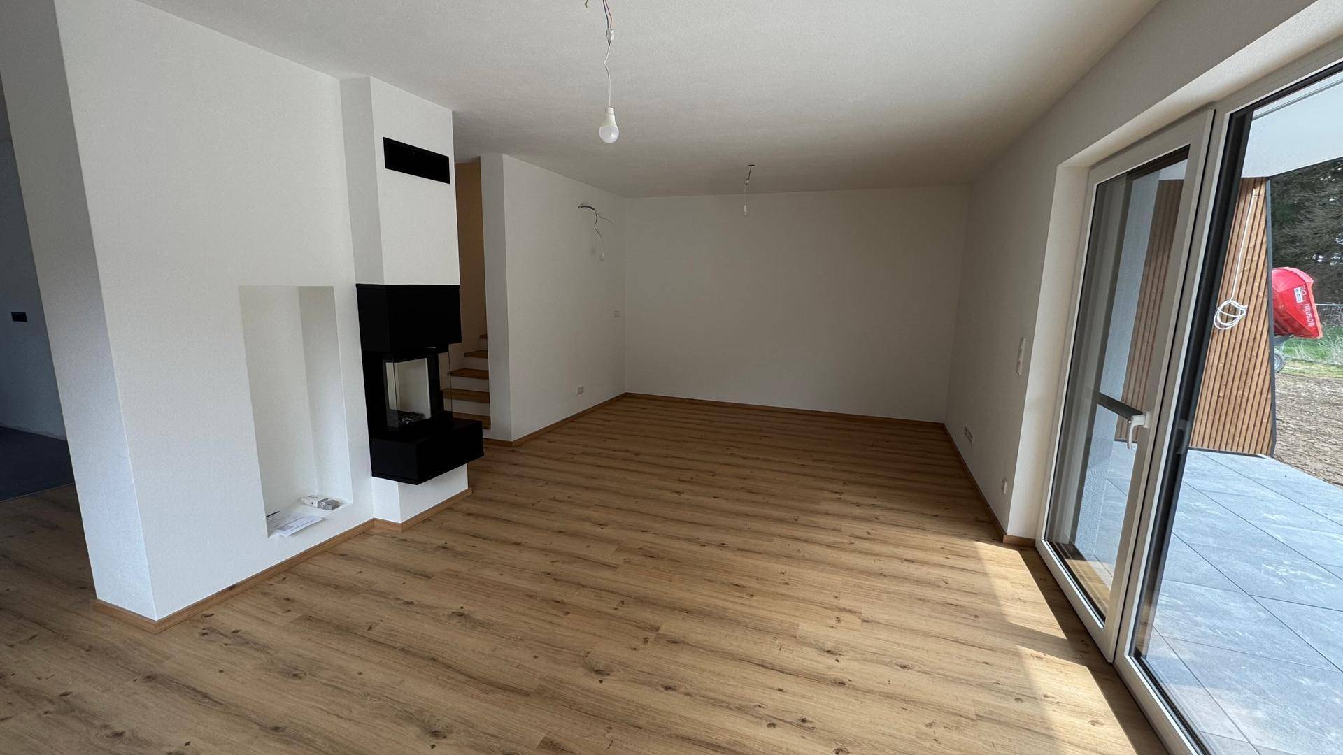 Geräumiges Wohnzimmer mit modernem Kamin, Holzboden und Zugang zur Terrasse.