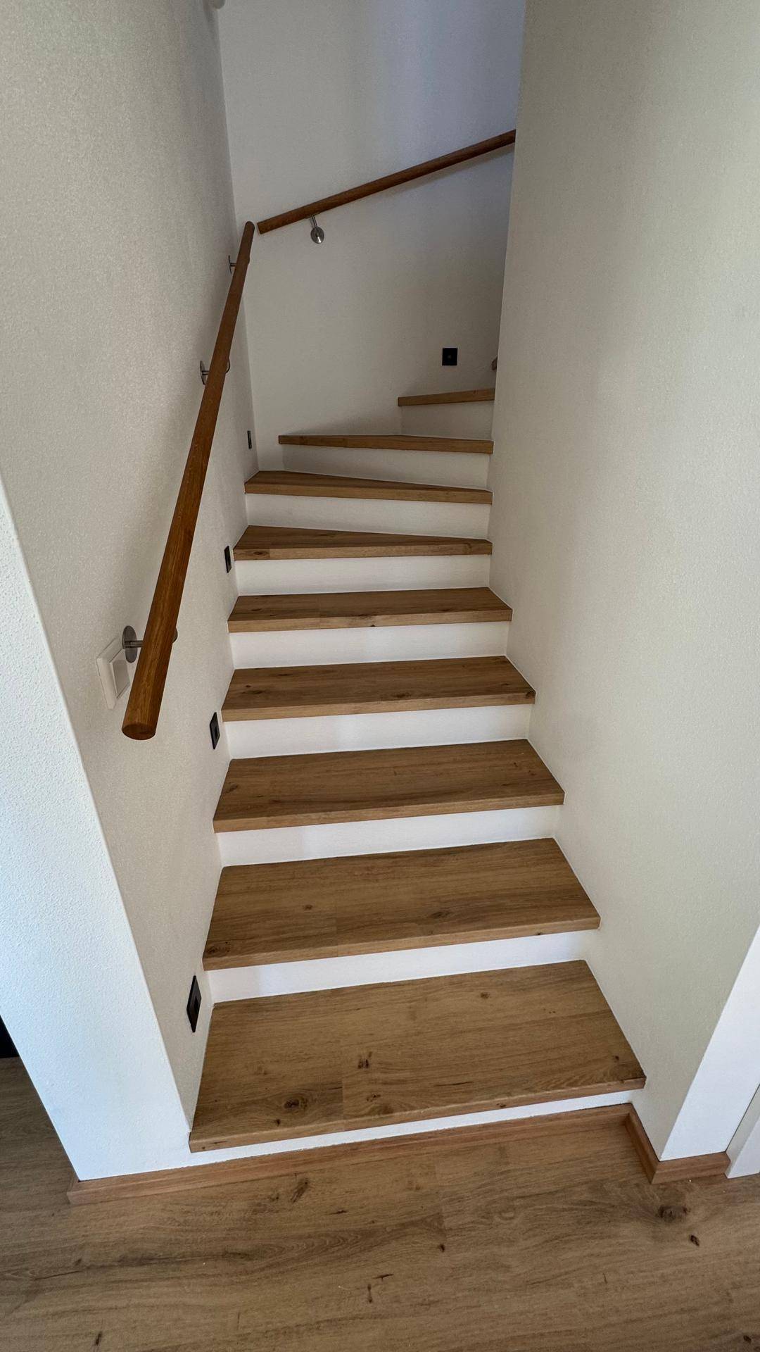 Helle Holztreppe mit weiß gestrichenen Setzstufen und passendem Holzgeländer.
