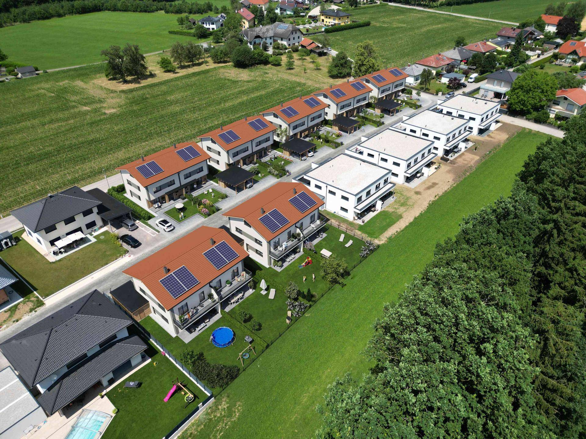 Luftaufnahme einer modernen Reihenhaussiedlung mit Gärten, Photovoltaikanlagen und umgebenden Grünflächen.