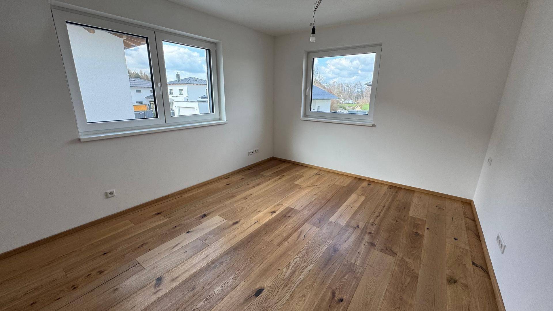 Helles Schlafzimmer mit zwei Fenstern und hochwertigem Holzplankenboden.