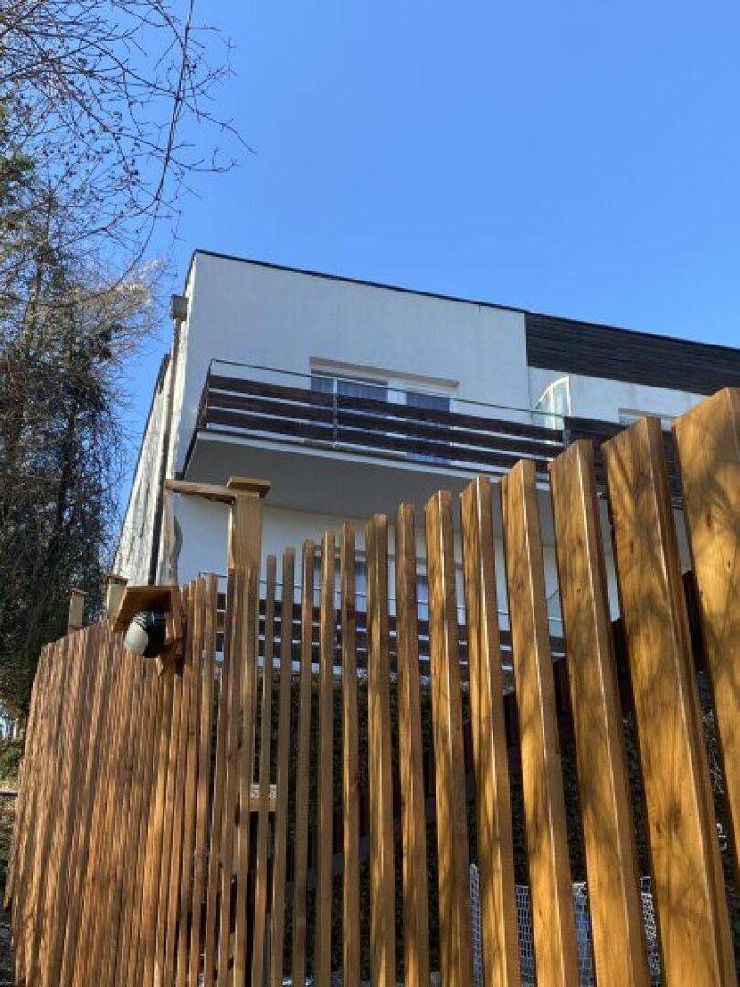 Moderne Gebäudefassade mit Balkon und einem stilvollen Holzzaun im Vordergrund.
