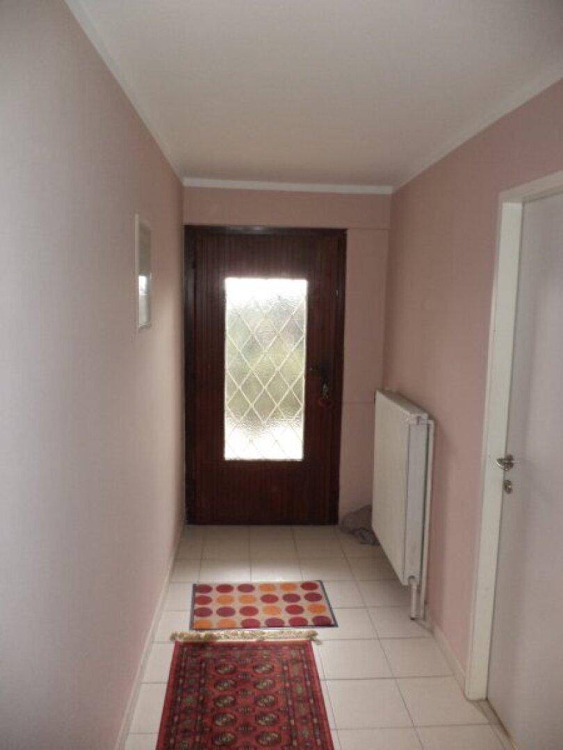 Eingangsbereich mit Fliesenboden, dunkler Holztür und einem Heizkörper an der Wand.