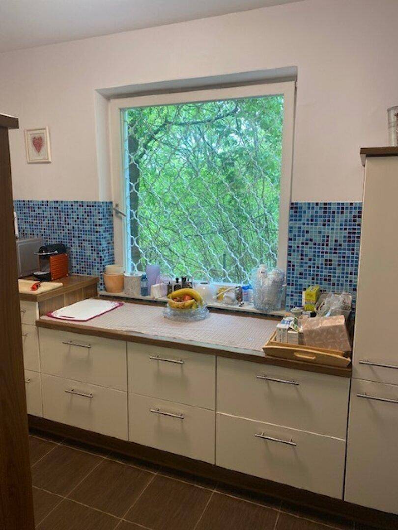 Helle Küche mit Fensterblick ins Grüne, weißen Unterschränken und blauen Fliesen.