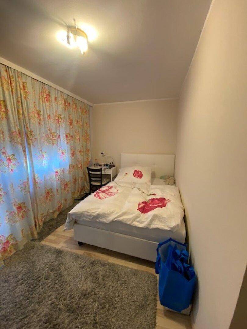 Kleines Schlafzimmer mit Einzelbett, hellem Boden und floralen Vorhängen.