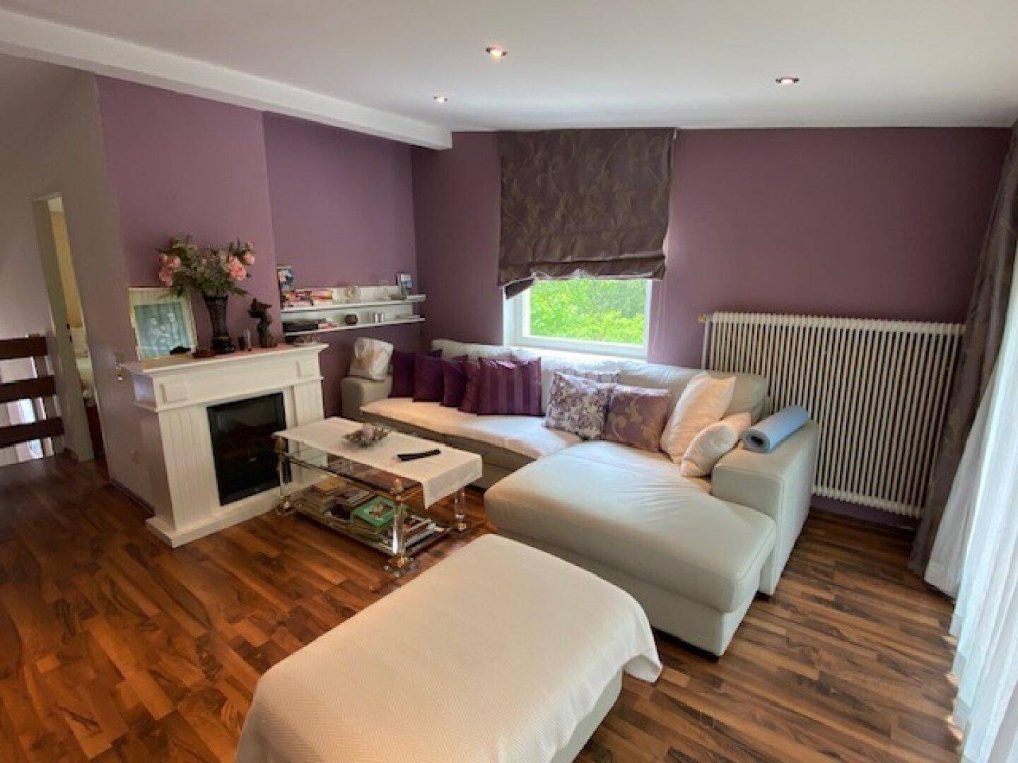 Wohnzimmer mit lila Wänden, Holzboden, Ecksofa und einem dekorativen Kamin.