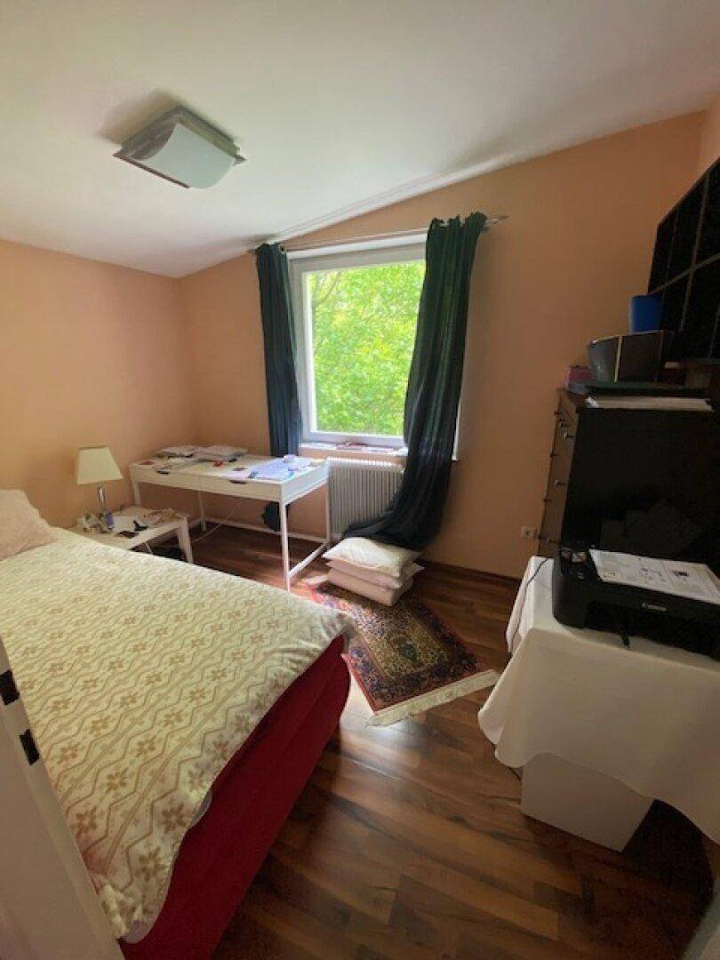 Schlafzimmer mit Holzboden, Einzelbett und Fenster mit Blick auf grüne Bäume.