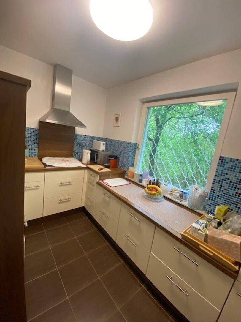 Funktionale Küche mit weißen Schränken, Holz-Arbeitsplatten und blauen Mosaikfliesen.